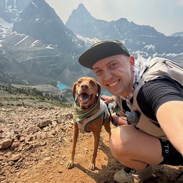 Evan Birch and Nova on an alpine trail with mountain peaks behind